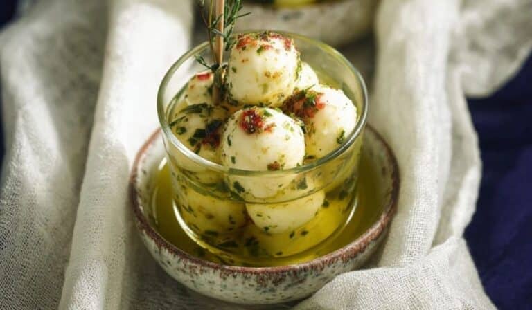 Marinated mozzarella balls in herb-infused olive oil served in a clear glass dish on a rustic tray