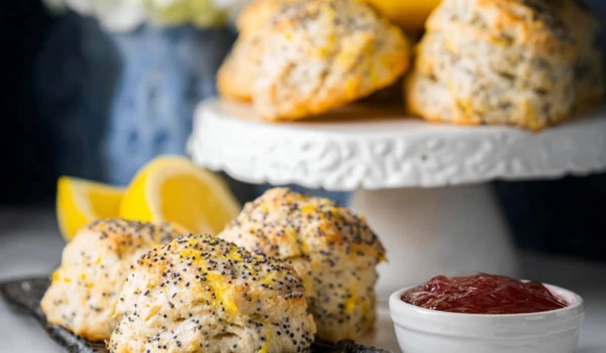 Freshly baked lemon poppy seed scones on a serving plate with lemon wedges and jam