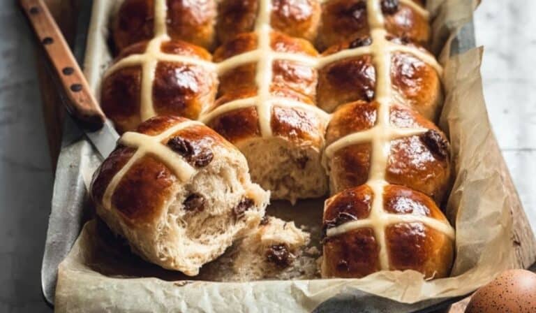 Homemade hot cross buns in a baking dish with glossy tops and soft crumb