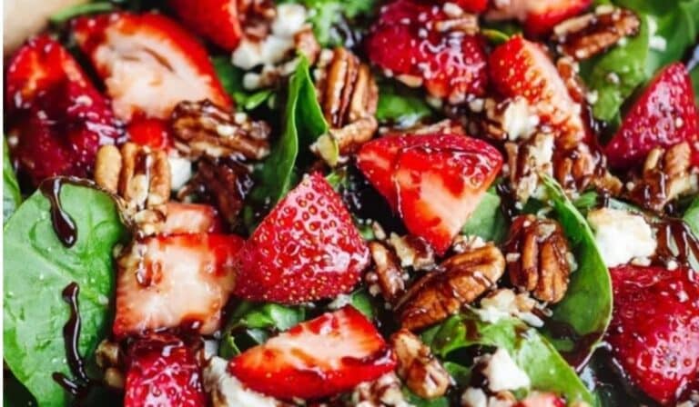 Strawberry spinach spring salad in a large bowl with berries, nuts, and goat cheese