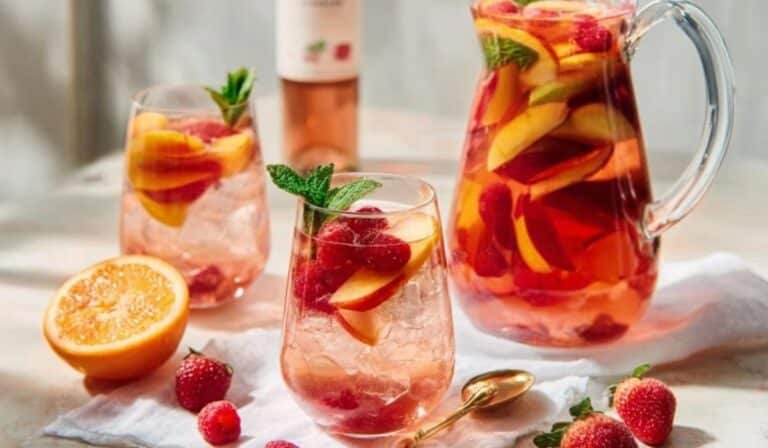 Rose sangria in a pitcher with peaches, berries, citrus, and mint
