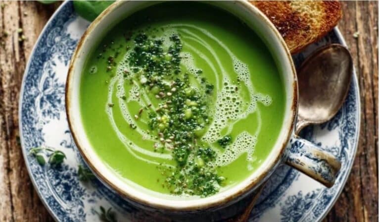 Spring green detox soup in a white bowl with peas, herbs, and lemon